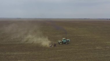 Aerial view tractor plows a large field. Dust in shot. Seagulls sits on field