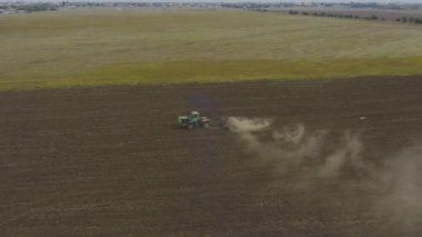 Aerial view tractor plows a dry field, dust flies behind