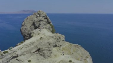 Denizde adanın kayalık pelerini. Kaya üzerinde turist yürüyüşü