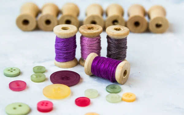 Bobina con hilos de colores y botones se encuentran sobre un fondo claro — Foto de Stock