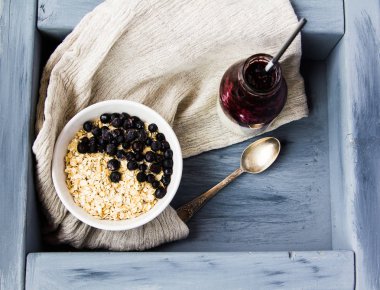 Gri bir tepsi üzerinde bir kase yulaf ezmesi ve yaban mersini, orada bir 