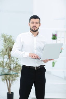 Genç işadamı ofiste dizüstü bilgisayarla çalışıyor.