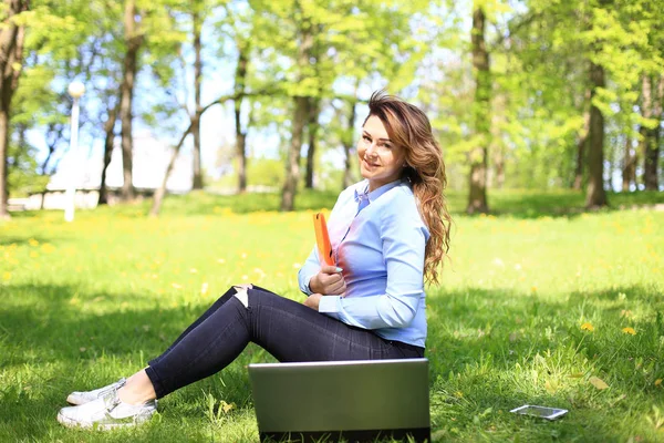 Giovane bella donna si trova sul prato verde estivo con computer portatile — Foto Stock