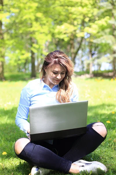 Giovane ragazza carina che lavora su laptop all'aperto, sdraiata sull'erba, caucasica 20 anni — Foto Stock