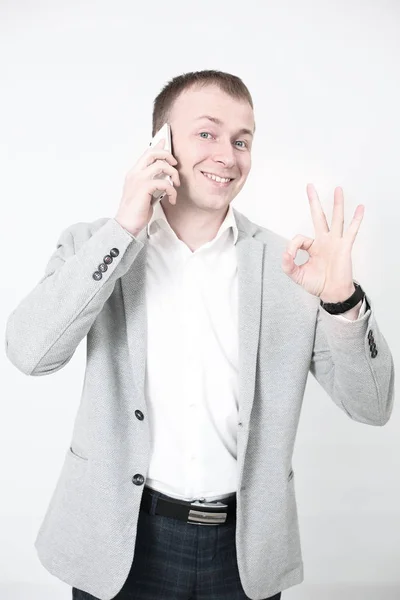 Улыбающийся молодой человек смотрит на свой смартфон, отправляя смс-ки на белом — стоковое фото