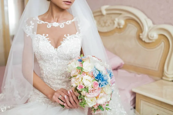 Nevěsta v šatech na posteli drží svatební kytice — Stock fotografie
