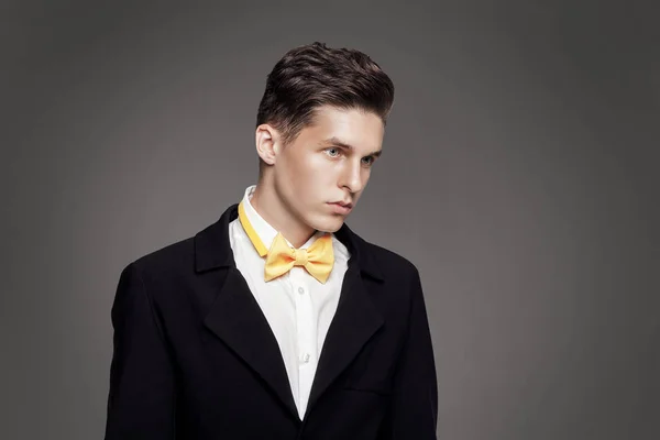 Trendy jongeman. Zwarte suite, gele bowtie, grijze achtergrond. Portret — Stockfoto