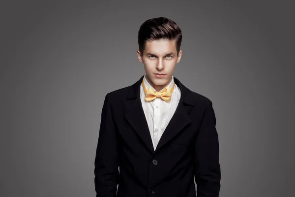 Young trendy man. Black suite, yellow bowtie, gray background. Portrait