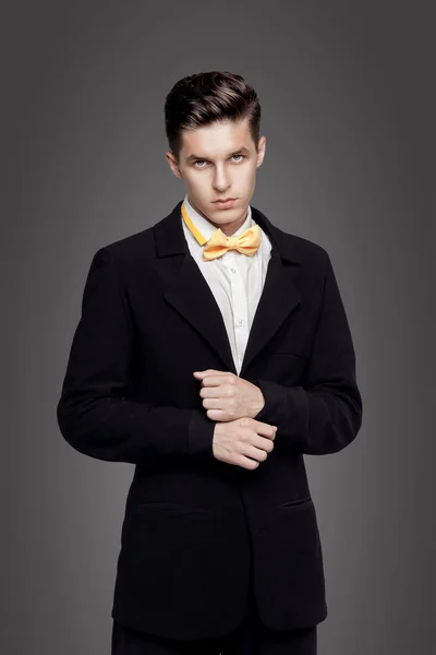 Unga trendiga mannen. Svart svit, gul bowtie, grå bakgrund. Porträtt — Stockfoto