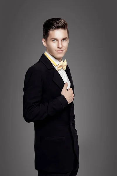 Trendy jongeman. Zwarte suite, gele bowtie, grijze achtergrond. Portret — Stockfoto