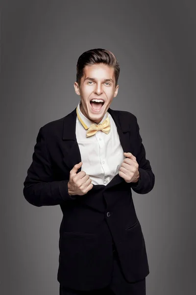 Trendy jongeman. Zwarte suite, gele bowtie, grijze achtergrond. Portret — Stockfoto