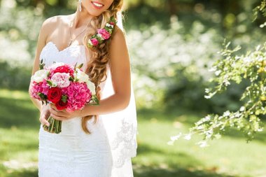 Gelin holding hassas evlilik buket. Park güzel güneşli bir günde.