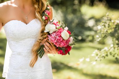 Gelin holding hassas evlilik buket. Park güzel güneşli bir günde.