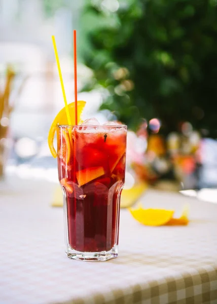 Red cocktail with straws and orange wedge in high glass