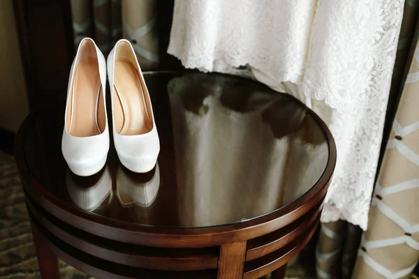 Lyxiga eleganta vita bröllop skor på träbord med en klänning i bakgrunden — Stockfoto