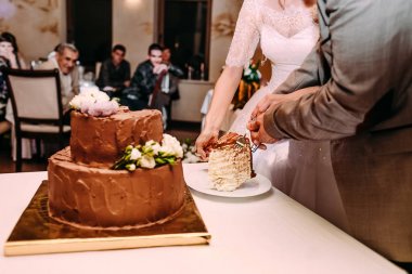 Gelin ve damat iki düzey kesme çikolatalı düğün pastası beyaz çiçeklerle dekore edilmiştir