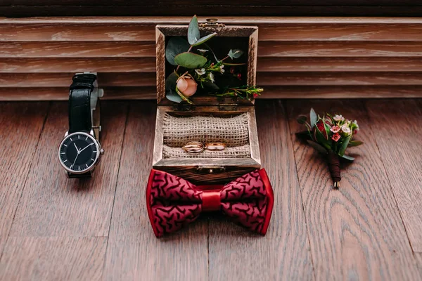 Eleganti accessori sposi su uno sfondo di legno. Papillon, boutonniere e anelli dorati . — Foto Stock