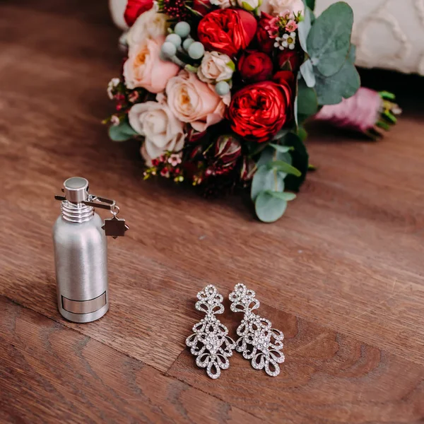 Krásné svatební náušnice a parfém na dřevěné podlaze vedle svatební kytice — Stock fotografie