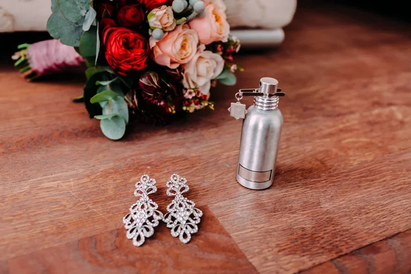 Belles boucles d'oreilles de mariée et parfum sur le sol en bois à côté du bouquet de mariage — Photo