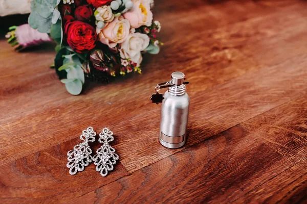 Brauteigenschaften wie elegante Silberohrringe mit Edelstein und Parfüm stehen neben dem Hochzeitsstrauß — Stockfoto