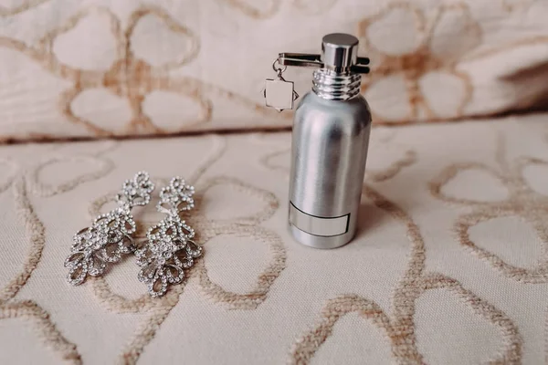 Atributos nupciais, como brincos de prata elegantes com gema e suporte de perfume no sofá leve — Fotografia de Stock