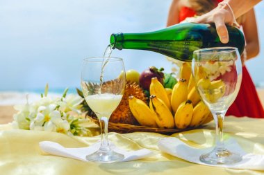 Adam içine bir tabak meyve ile bir arka plan üzerine bir bardak şampanya döküyor. Kutlama sahilde