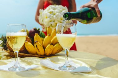 Adam içine bir tabak meyve ile bir arka plan üzerine bir bardak şampanya döküyor. Kutlama sahilde