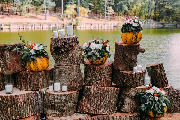 Beautiful wedding decoration autumn wedding in orange colors. An outdoor ceremony near a lake. Pumpkins, flowers, and candles