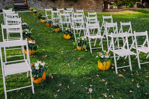 婚礼装饰用秋天的南瓜和鲜花。在公园户外仪式。客人的白色椅子 — 图库照片