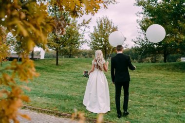 Güzel gelin ve Damat Düğün gününde ellerinde beyaz balonlarla yeşil çimenlerin üzerinde duran.