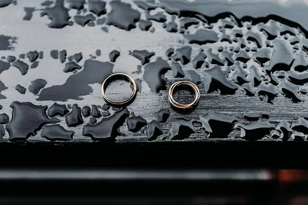 Anillos de boda sobre fondo de madera oscura con gotas de agua. Joyas inusuales Foto —  Fotos de Stock