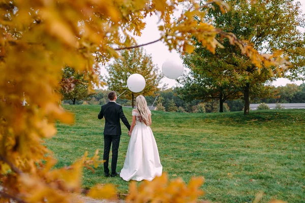 Felice sposa e lo sposo avendo un grande momento in piedi sull'erba verde con palloncini bianchi nelle loro mani il giorno del loro matrimonio . — Foto Stock
