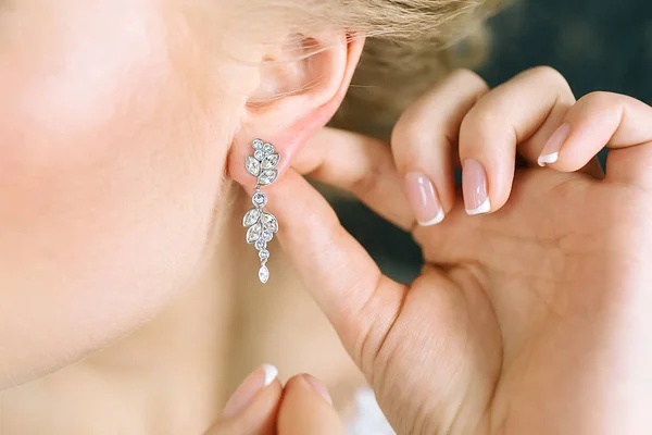 Elegant blonde bride putting on earrings, preparing for the wedding. Close-up — Stock Photo, Image