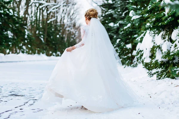 Hermosa novia corriendo en el bosque nevado, agitando su vestido en un día de boda. Vista trasera. Ceremonia de invierno — Foto de Stock