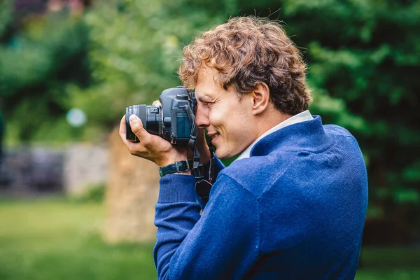 Een lachende man met een camera. Een fotograaf maakt buiten foto 's. Close-up portret van de fotograaf in actie. — Stockfoto