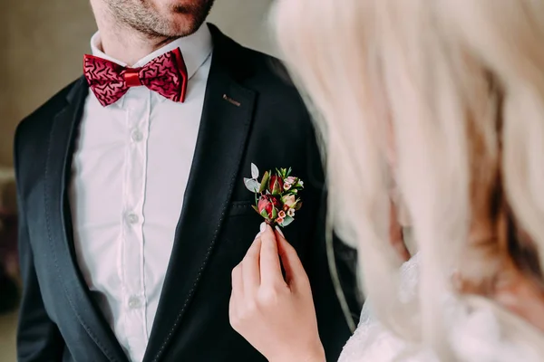 Ślubne. Zbliżenie narzeczonej ręce Przypinanie boutonniere wobec szambelan królewski ' kurtka. Nieostrość na boutonniere — Zdjęcie stockowe