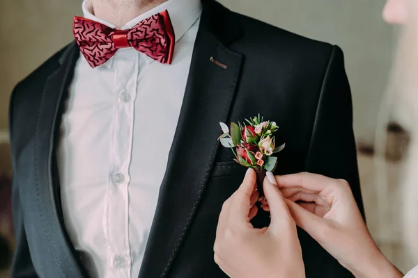 Bröllop. Närbild av brudens händer fästa boutonniere till groom' jacka. Mjukt fokus på boutonniere — Stockfoto