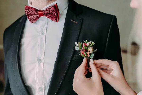 Ślubne. Zbliżenie narzeczonej ręce Przypinanie boutonniere wobec szambelan królewski ' kurtka. Nieostrość na boutonniere — Zdjęcie stockowe