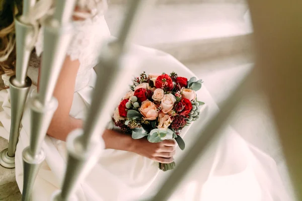 Beau bouquet de mariée avec des roses blanches et pêche, pivoines rouges, et d'autres fleurs. Le matin du mariage. La mariée tient un bouquet de fleurs et est assise dans les escaliers. Oeuvres — Photo