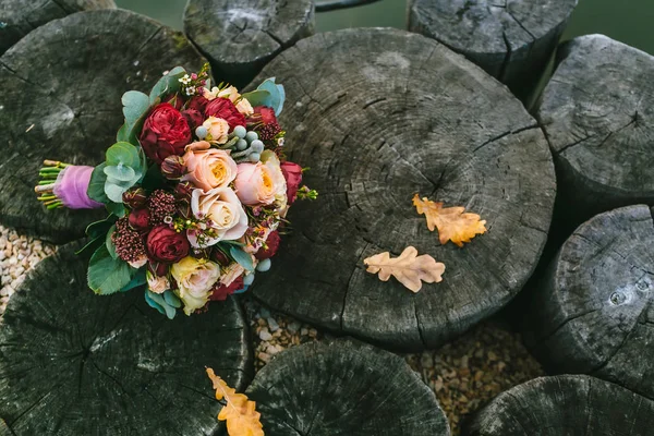 Hochzeitsstrauß der Farbe Marsala liegt auf einem hölzernen Hintergrund. schöner Blumenstrauß mit weißen und pfirsichfarbenen Rosen, rote Pfingstrosen liegen auf gealterten Baumstämmen. — Stockfoto