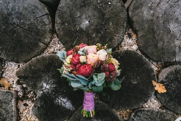 Hochzeitsstrauß der Farbe Marsala liegt auf einem hölzernen Hintergrund. schöner Blumenstrauß mit weißen und pfirsichfarbenen Rosen, rote Pfingstrosen liegen auf alten Baumstämmen. — Stockfoto