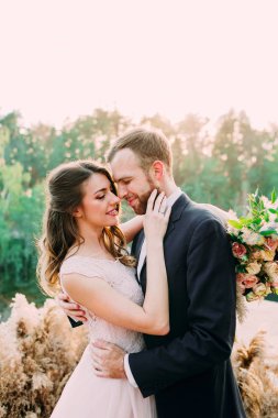 Sevecen yeni evlilerin burunlarına dokunan portresi. Gelin ve damat doğada poz veriyor. Düğün.