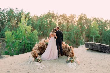 Yeni evliler kanyonun kenarında şefkat ve sevgiyle kucaklaşıyorlar. Arkadan bak. Açık hava düğünü