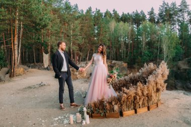 Yeni evliler el ele tutuşuyor, gülüyor ve gülümsüyor, mutlu ve neşeli anlar. Gelin ve damat doğada yürüyor. Açık hava düğünü