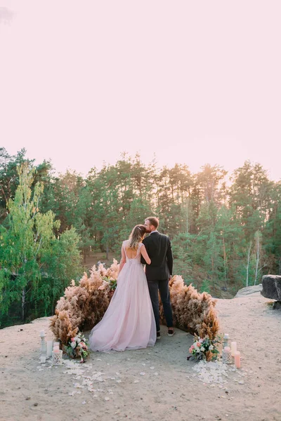 Yeni evliler kanyonun kenarında şefkat ve sevgiyle kucaklaşıyorlar. Arkadan bak. Açık hava düğünü