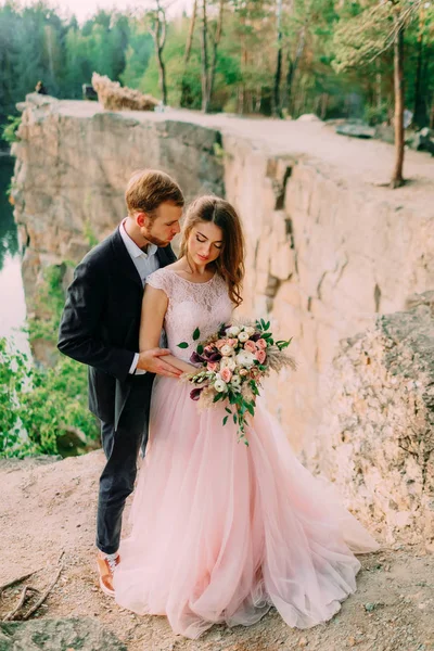 Felizes recém-casados abraçando. Homem em tuxedo e mulher em um vestido de noiva rosa está posando sobre a natureza. Cerimônia ao ar livre. Close-up — Fotografia de Stock