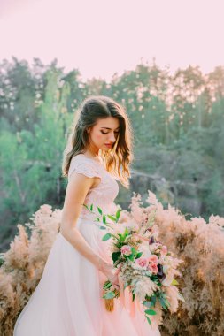 Kır gelini buketi olan gelin kayanın üzerinde duruyor. Düğün töreni, dekorasyon.