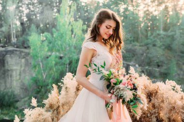 Kır gelini buketi olan gelin kayanın üzerinde duruyor. Düğün töreni, dekorasyon.