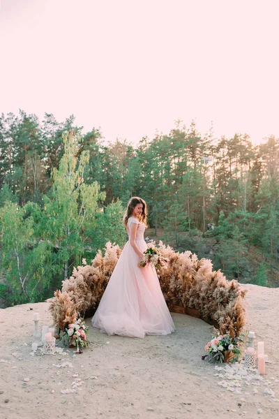 素朴なブライダル花束を持つ花嫁が岩の上に立っています。結婚式、装飾 — ストック写真