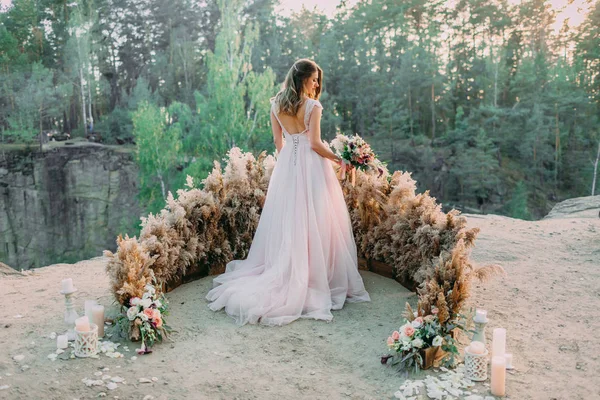 素朴なブライダル花束を持つ花嫁が岩の上に立っています。結婚式だ。バックビュー — ストック写真